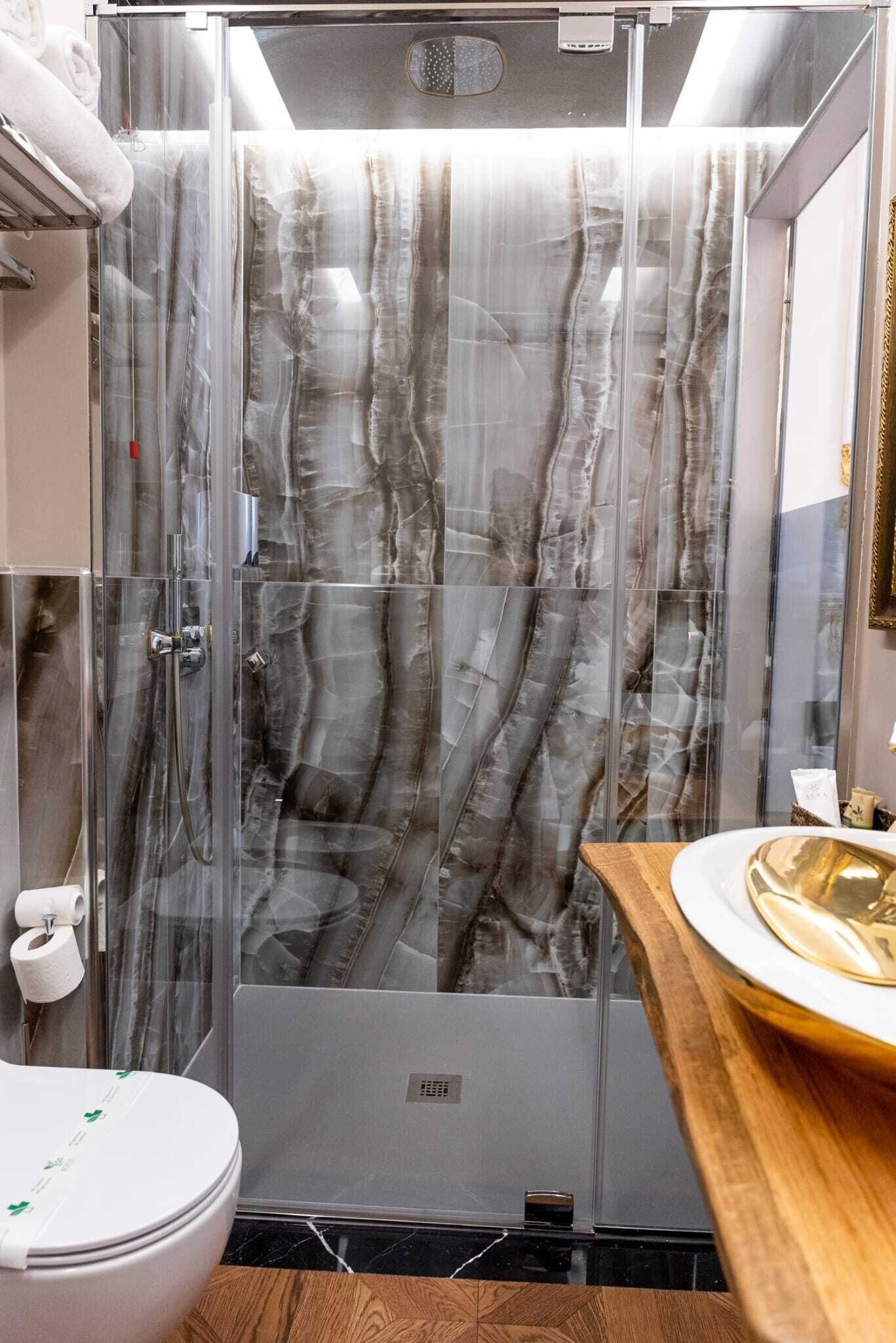 A bathroom with a glass shower enclosure, a toilet, and a sink with a marble countertop.