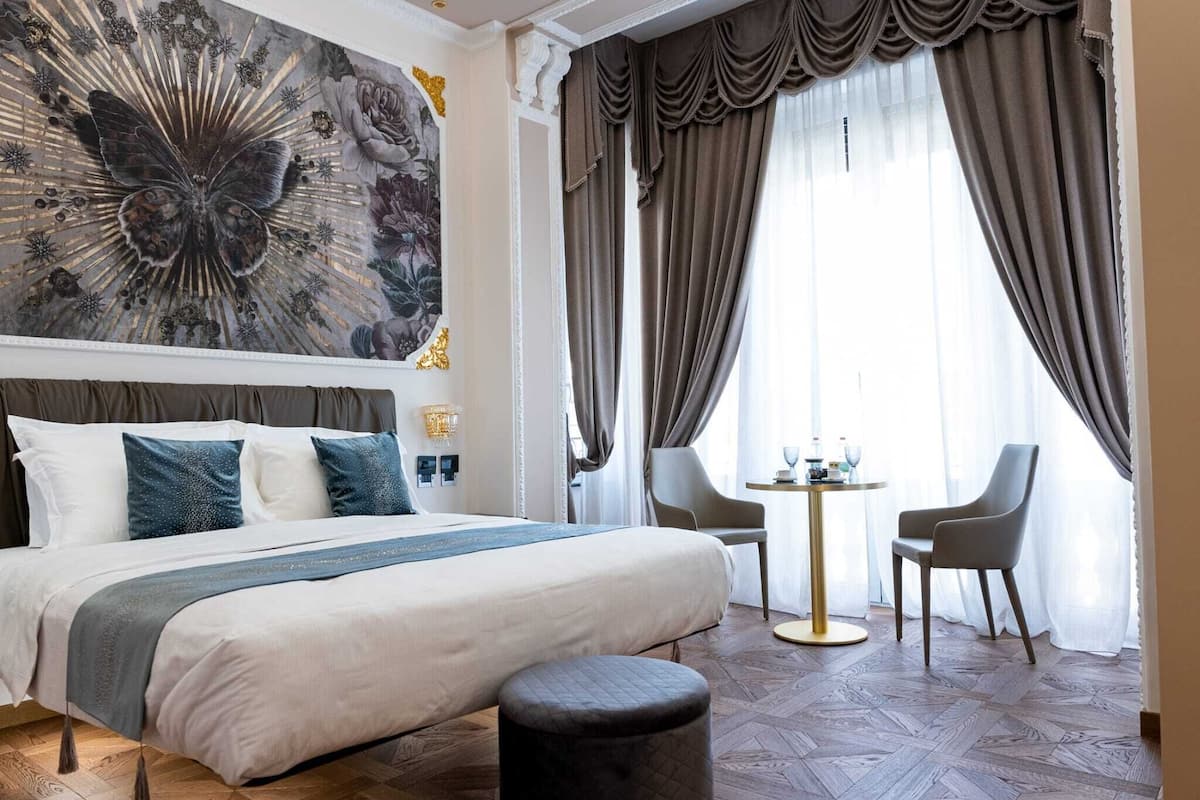 Ein Hotelzimmer mit einem großen Bett, einem runden Tisch, zwei Stühlen und einem dekorativen Wandgemälde.