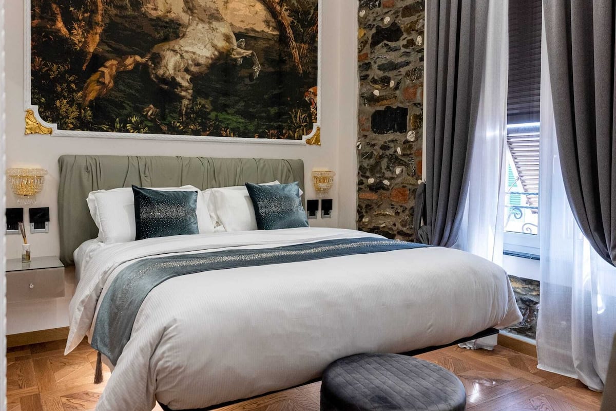 Ein Schlafzimmer mit einem großen Bett, einer Steinwand, einem Gemälde und einem Fenster mit Vorhängen.
