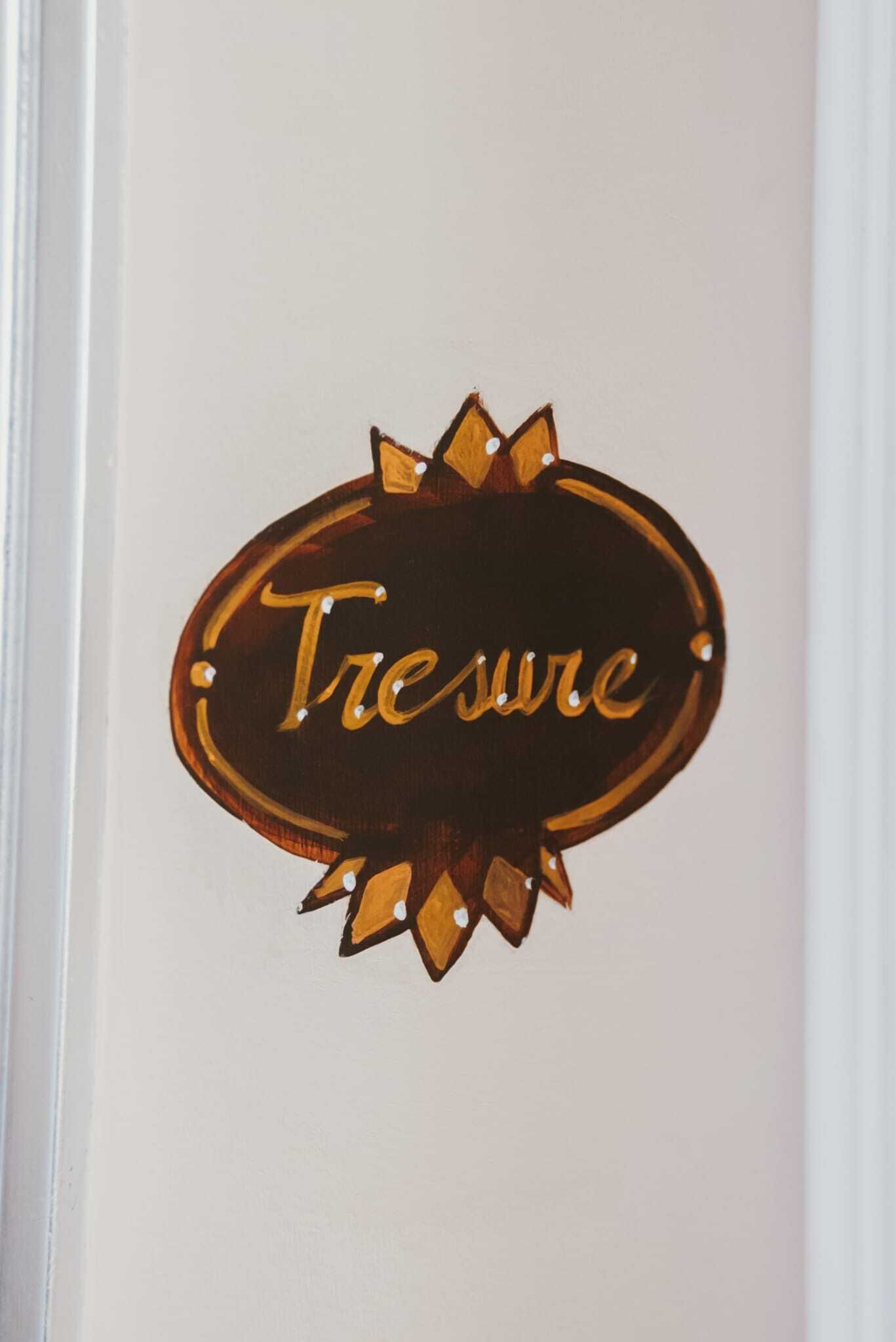 A wooden sign with the word "Tresure" on a white wall.
