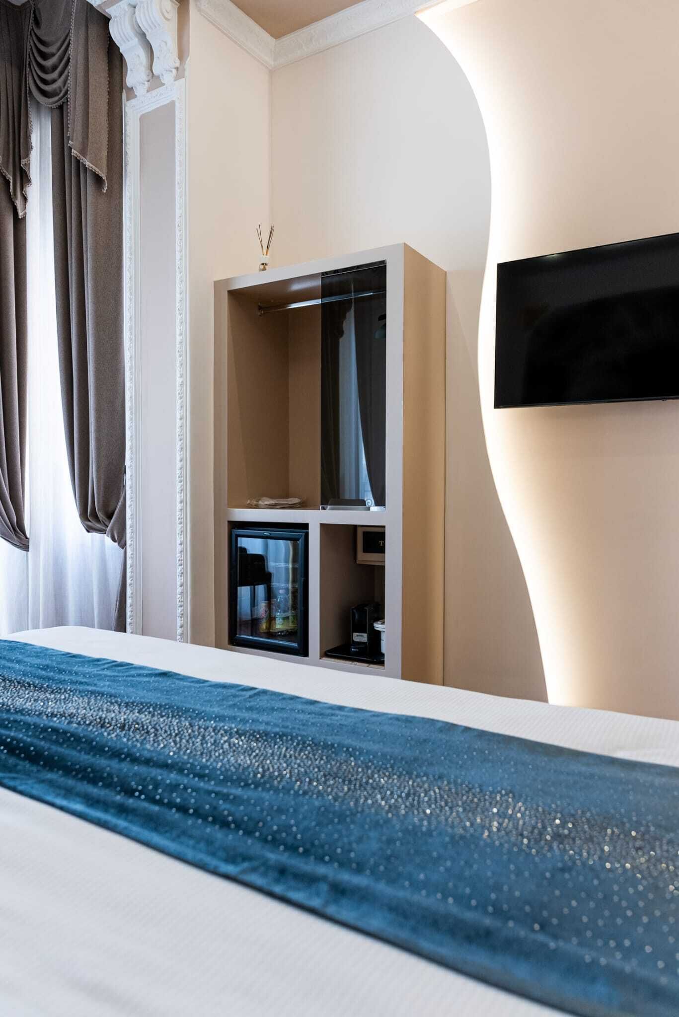 A hotel room with a bed, a minibar, a television mounted on the wall, and a window with curtains.
