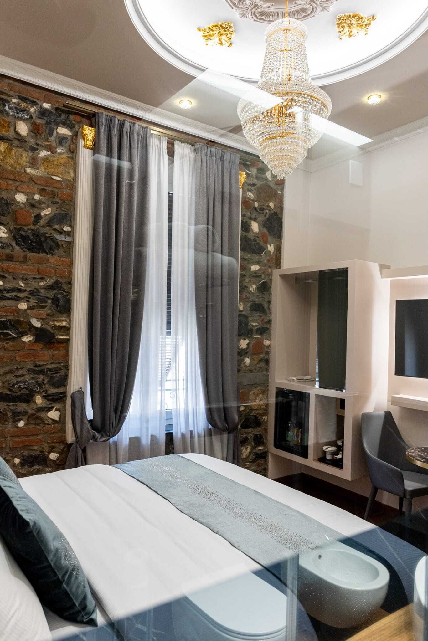 A modern bedroom with a stone accent wall, a large bed with a headboard, a chandelier, and a television on a stand.