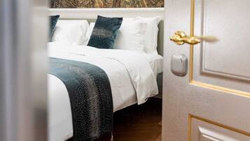 A bedroom with a bed, white bedding, a dark blue throw, and a wall with a floral tapestry.