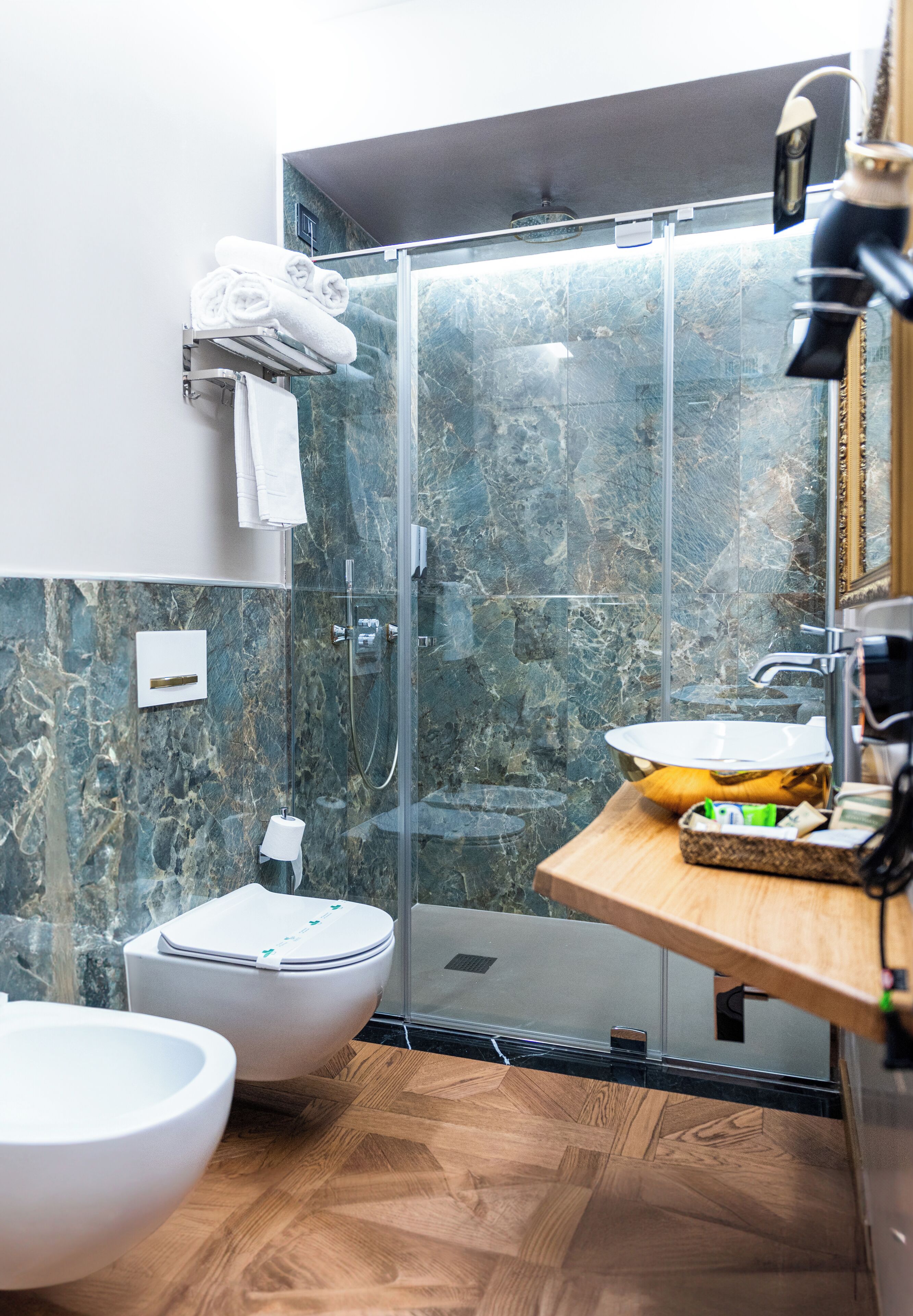 Un bany modern amb dutxa de vidre, un vàter i un lavabo amb taulell de fusta.