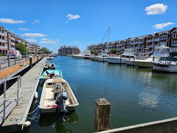Uma marina com barcos atracados, um cais de madeira e edifícios ao fundo.