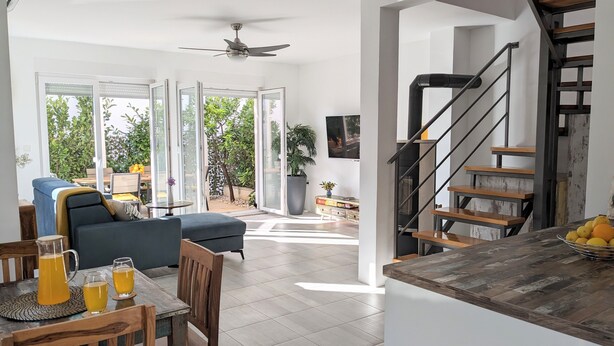A spacious living area with a dining table, chairs, and a sofa. There is a staircase leading to an upper level.