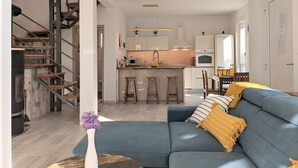 A modern living room with a blue sofa, a wooden staircase, and a kitchen area with white cabinets and a central island.