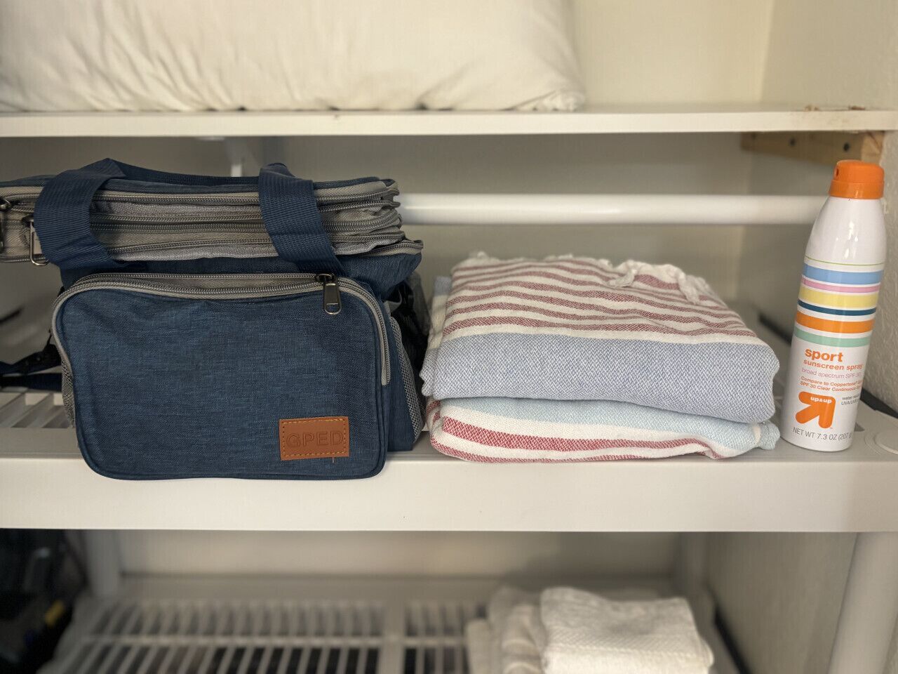 A shelf with a denim bag, folded towels, and a sunscreen bottle.