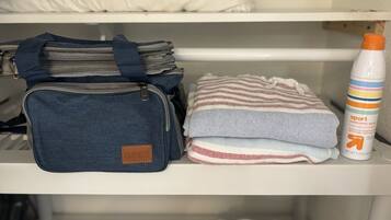 A shelf with a denim bag, folded towels, and a sunscreen bottle.