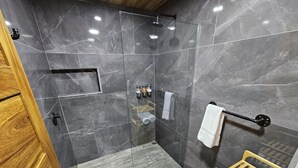 Un baño moderno con ducha de vidrio, detalles de madera y toallero empotrado.