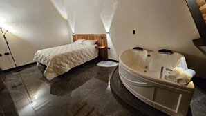Un dormitorio moderno con una cama grande, cabecera de madera, bañera integrada y una mesita de noche pequeña.