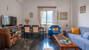 Un salon comprenant un téléviseur, des étagères, une table basse, un canapé et un coin repas avec des chaises et une table.