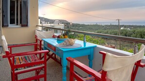 Un balcon avec une table bleue et des chaises rouges, donnant sur un paysage pittoresque.
