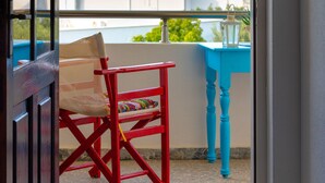 Un balcon avec une chaise rouge, une table bleue et une vue sur la mer.