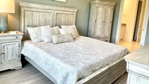 A bedroom with a large bed, a nightstand, a dresser, and a painting on the wall.