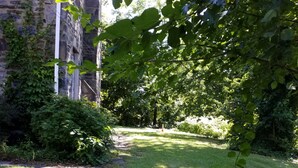 A stone pathway leading through a grassy area with dense foliage and a stone building in the background. - Fairmount House at The Mann (Philadelphia)