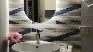 A bathroom with a large oval mirror, a sink, a vase with pink flowers, and a patterned wall.