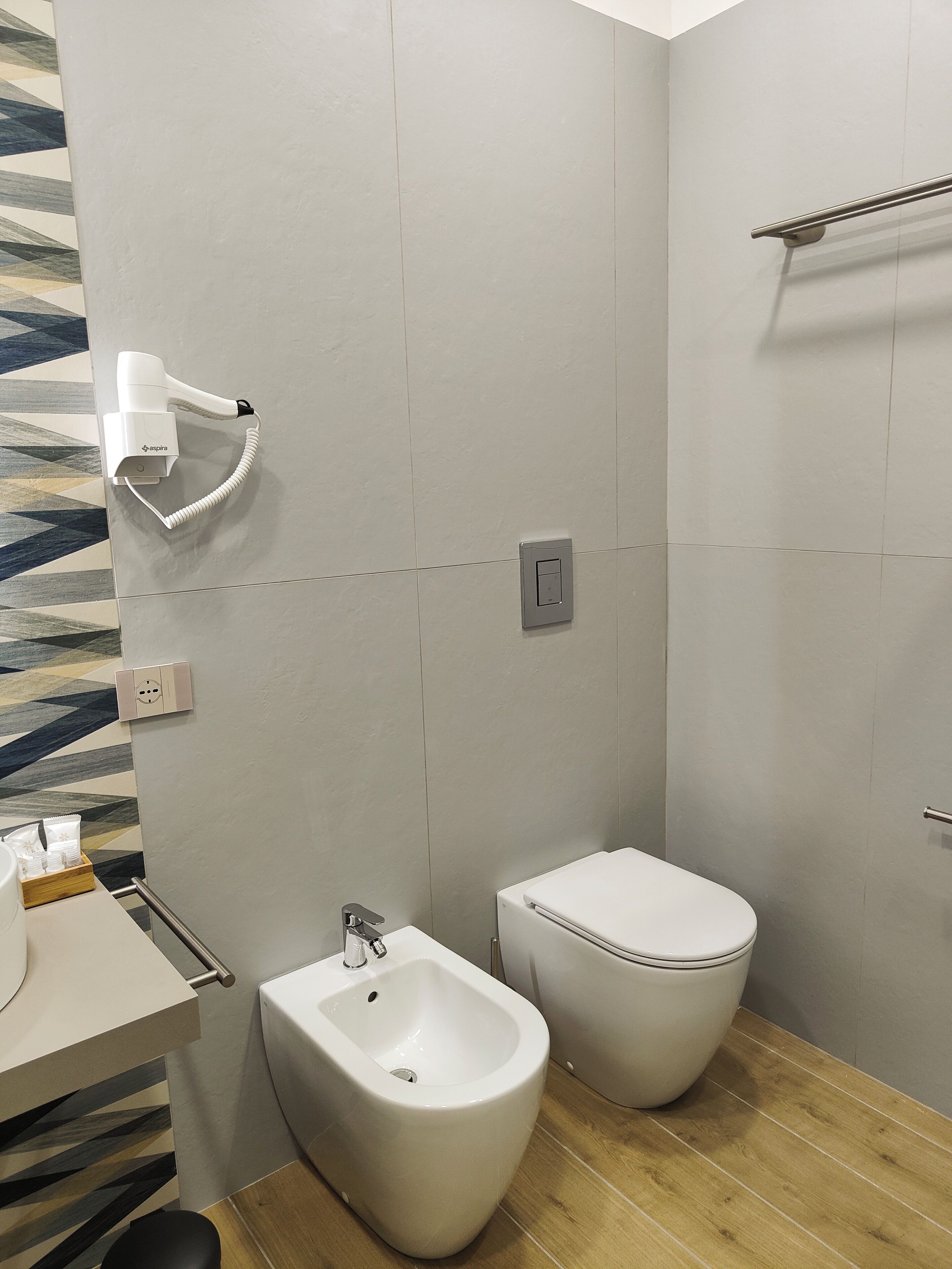 A modern bathroom with a bidet, toilet, and hair dryer mounted on the wall.