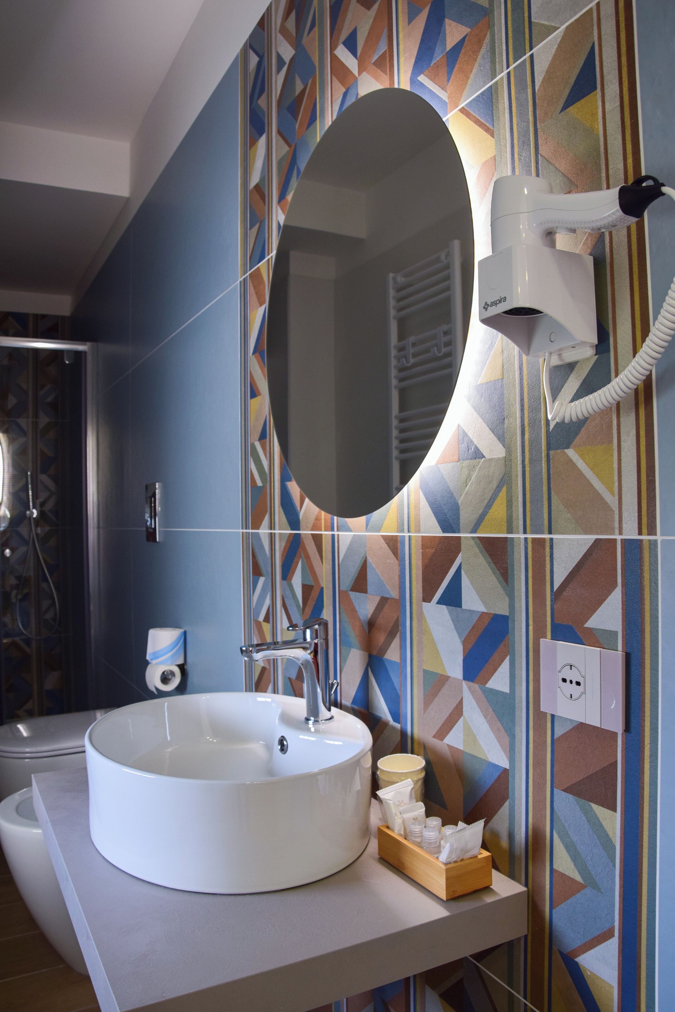 Un baño con un lavabo blanco redondo, un espejo y un secador de pelo montado en la pared.