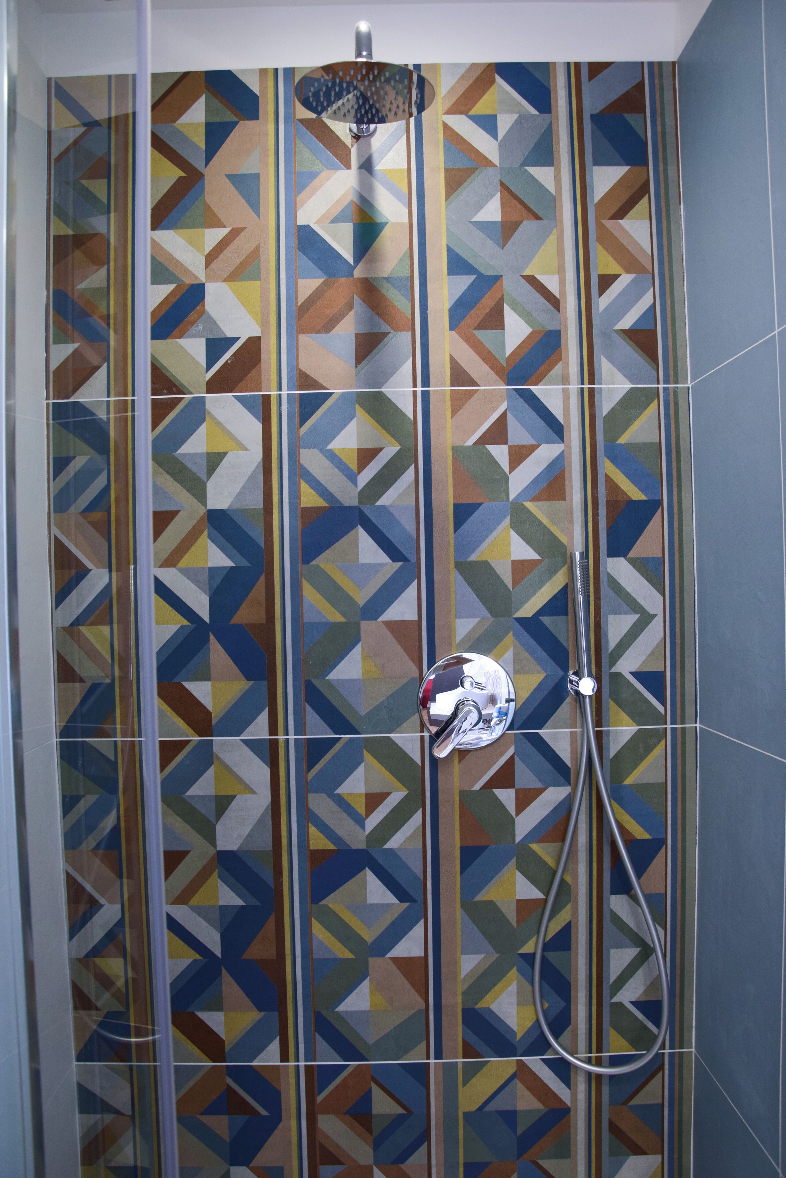 A shower with a geometric tile pattern and a handheld showerhead.
