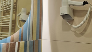 A bathroom with a striped towel rack, a hairdryer mounted on the wall, and a power outlet.