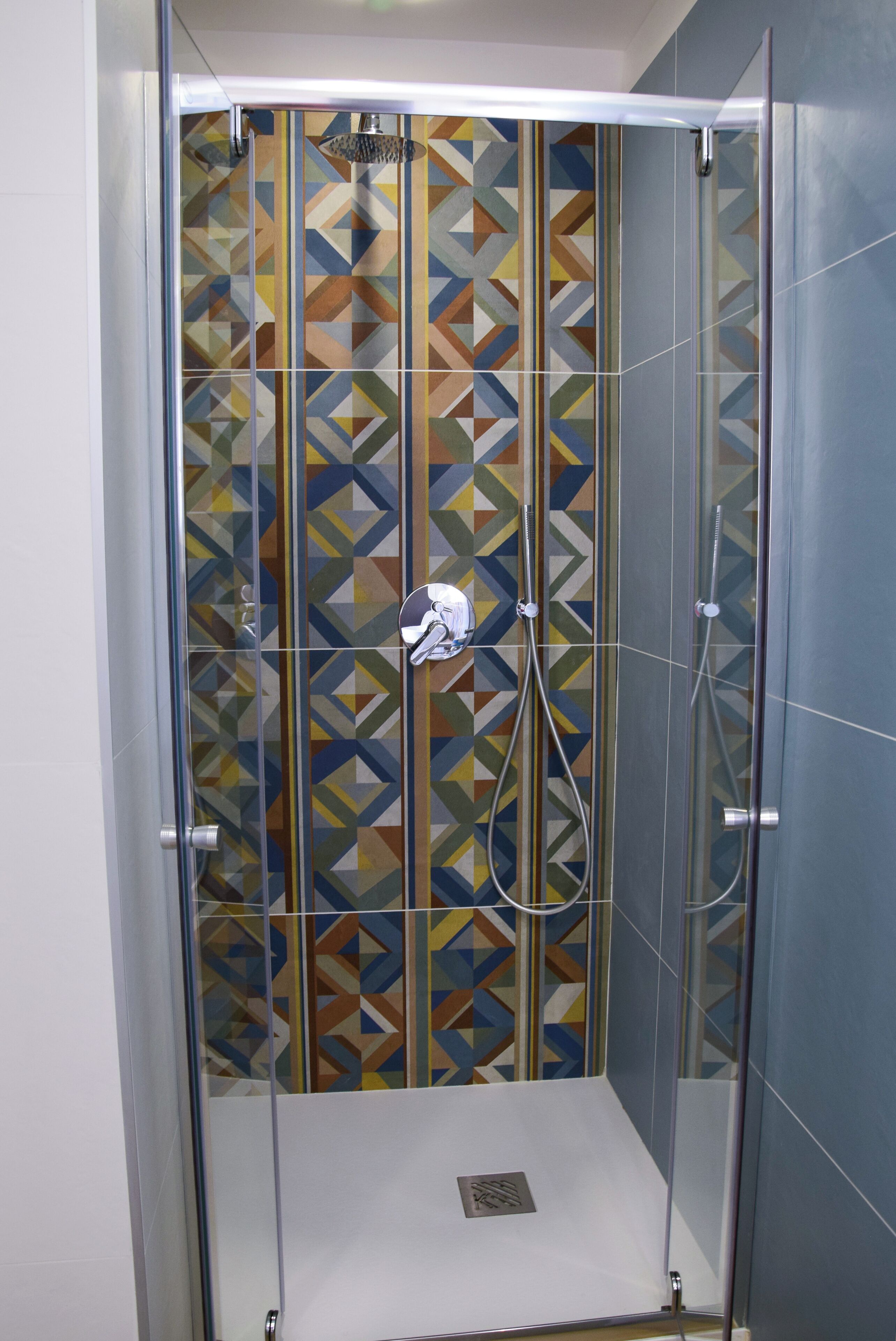 A glass-enclosed shower with a geometric tile backsplash.