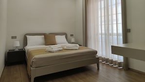 A modern bedroom with a bed, bedside tables, a desk, and a large window with curtains.
