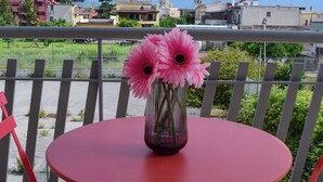 A red table with a vase of pink flowers on a balcony overlooking a cityscape with mountains in the background.