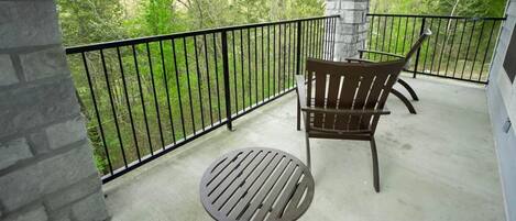 A balcony with a round table and two chairs, a stone pillar, and a black railing.