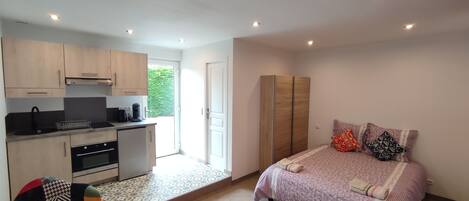 A compact room with a kitchenette, a bed with patterned bedding, and a door leading to a balcony.