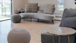 Una sala moderna con un sofá gris, un taburete redondo y una pequeña mesa circular.