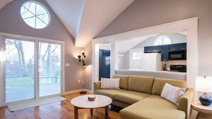 Una sala de estar moderna con un sofá, una mesa de centro y una lámpara. Hay un ventanal y vistas al exterior.