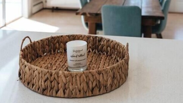 Un área de comedor con una mesa y sillas de madera, una bandeja tejida con una vela, y un candelabro moderno.