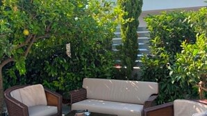 Un área de estar al aire libre con mobiliario de mimbre, piso de piedra y abundante vegetación.