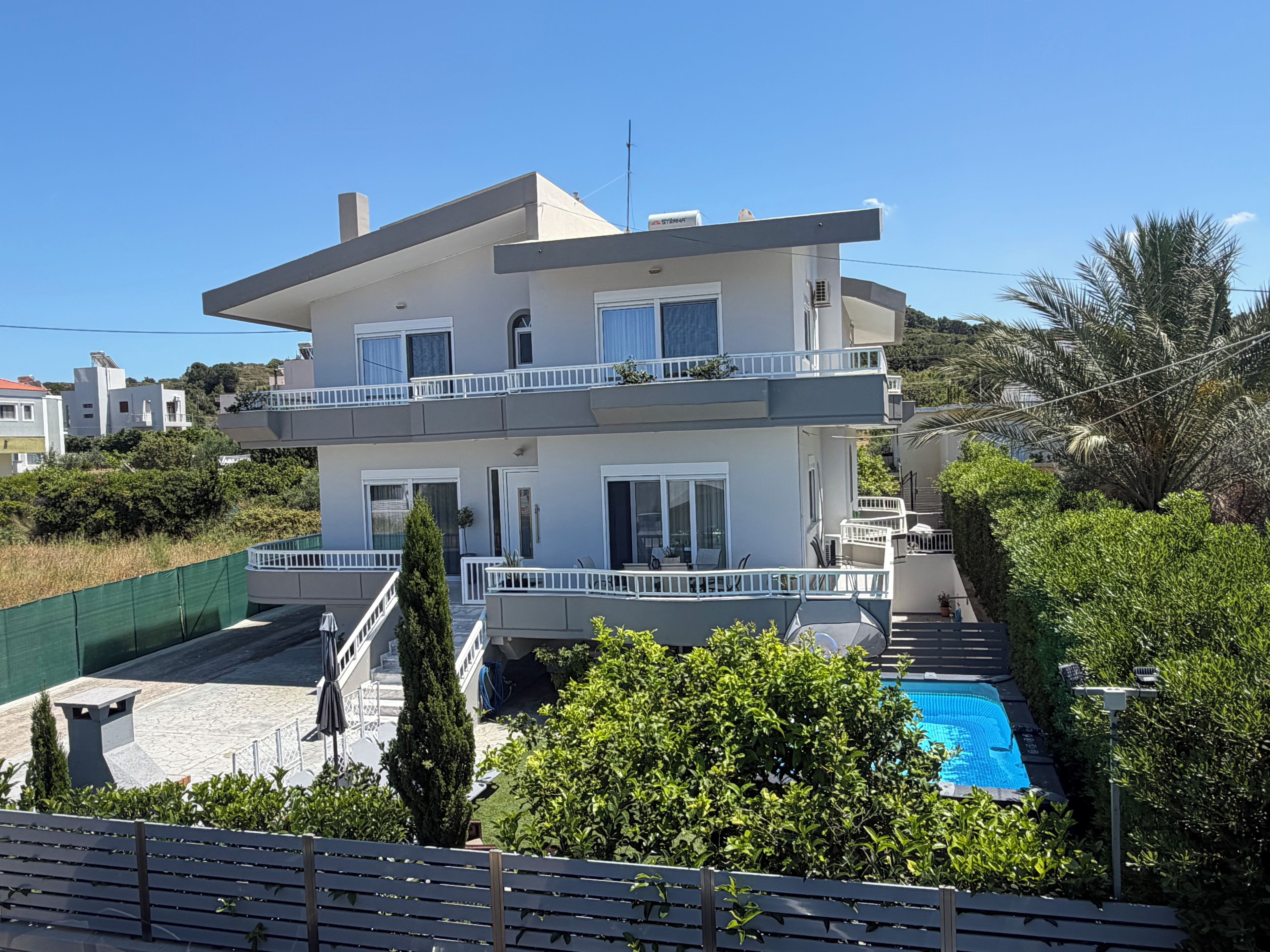 Edifici d'apartaments de diversos pisos amb balcons, piscina i vegetació als voltants.