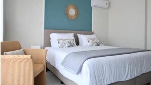 Habitación de hotel con cama, una silla, aire acondicionado instalado en la pared y un espejo decorativo.