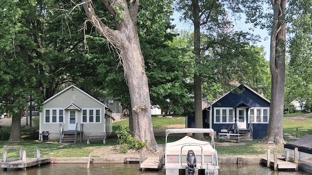 Una cabaña frente al lago con un muelle, un bote pequeño y una mesa de picnic.