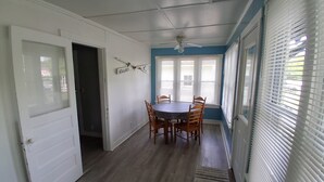 Un comedor con una mesa redonda y sillas, un ventilador de techo y vistas a través de las ventanas.