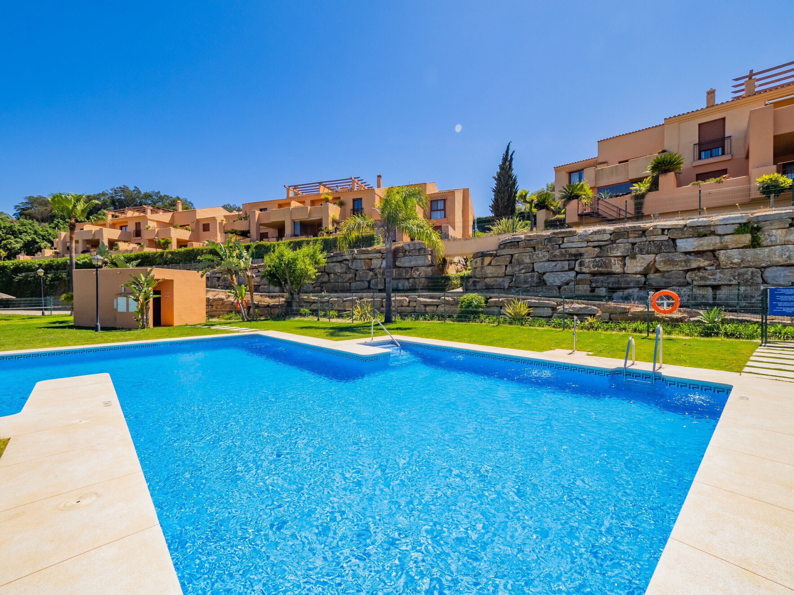 A swimming pool with a stone wall and a clear blue sky.