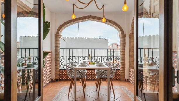 An outdoor dining area with a table set for four, surrounded by white chairs, under a brick archway with hanging lights. - casa carpa andalucia II (Nerja)