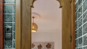 A room with a wooden door leading to a bed with a patterned headboard, a hanging light fixture, and a tiled wall. - casa carpa andalucia II (Nerja)