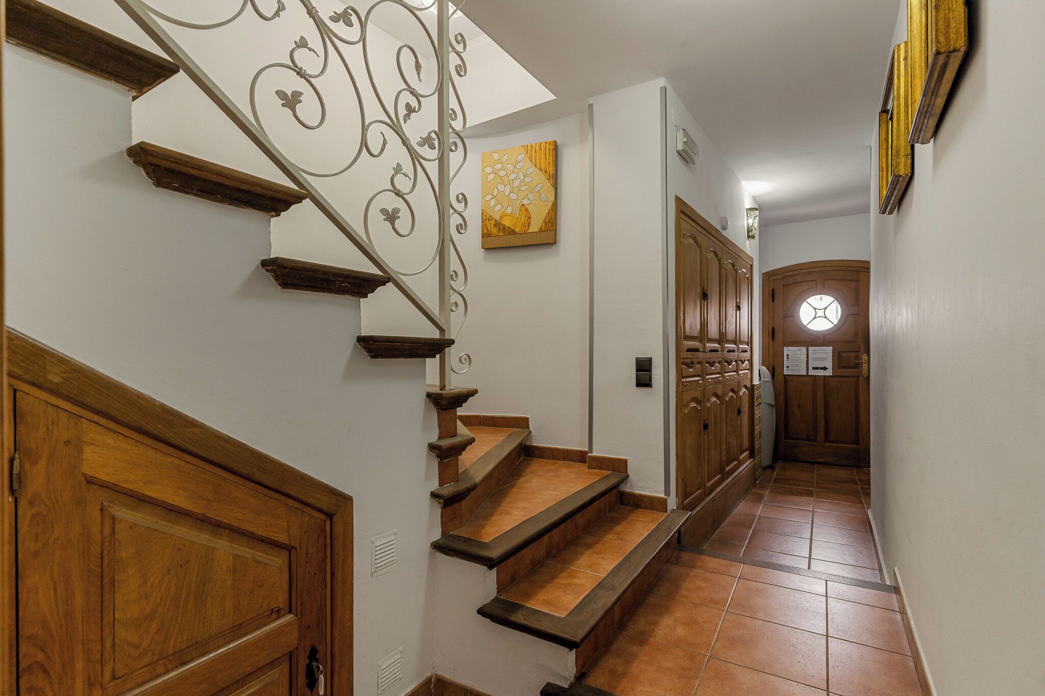 Un escalier avec des marches en bois et une rampe en métal, menant à une pièce dotée d’une porte en bois et d’une fenêtre circulaire.