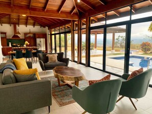A spacious living area with a modern design, featuring a large window with a view of a swimming pool and landscape. - Exclusive Atenas Oasis, Breathtaking Views, Heated Pool & Jacuzzi, AC bedrooms (Atenas)