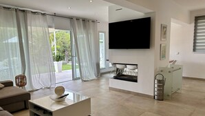 En moderne stue med et fladskærms-tv ophængt på væggen, en pejs og en skydedør, der fører ud til en balkon.