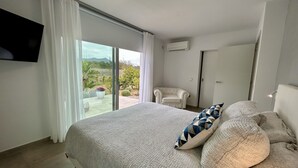 Et soveværelse med en stor seng, et TV ophængt på væggen og en skydedør, der fører ud til en balkon.