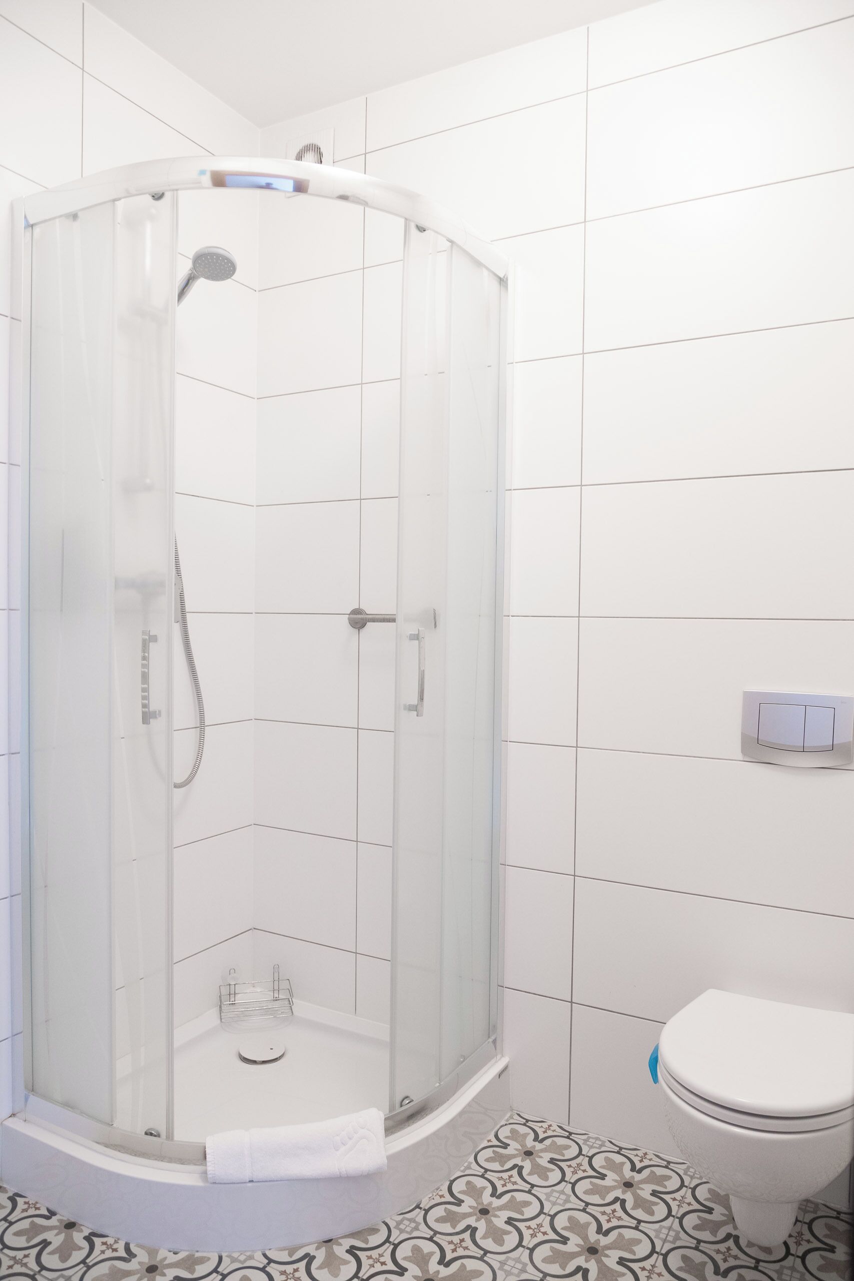 A modern bathroom with a glass-enclosed shower, a toilet, and patterned floor tiles.
