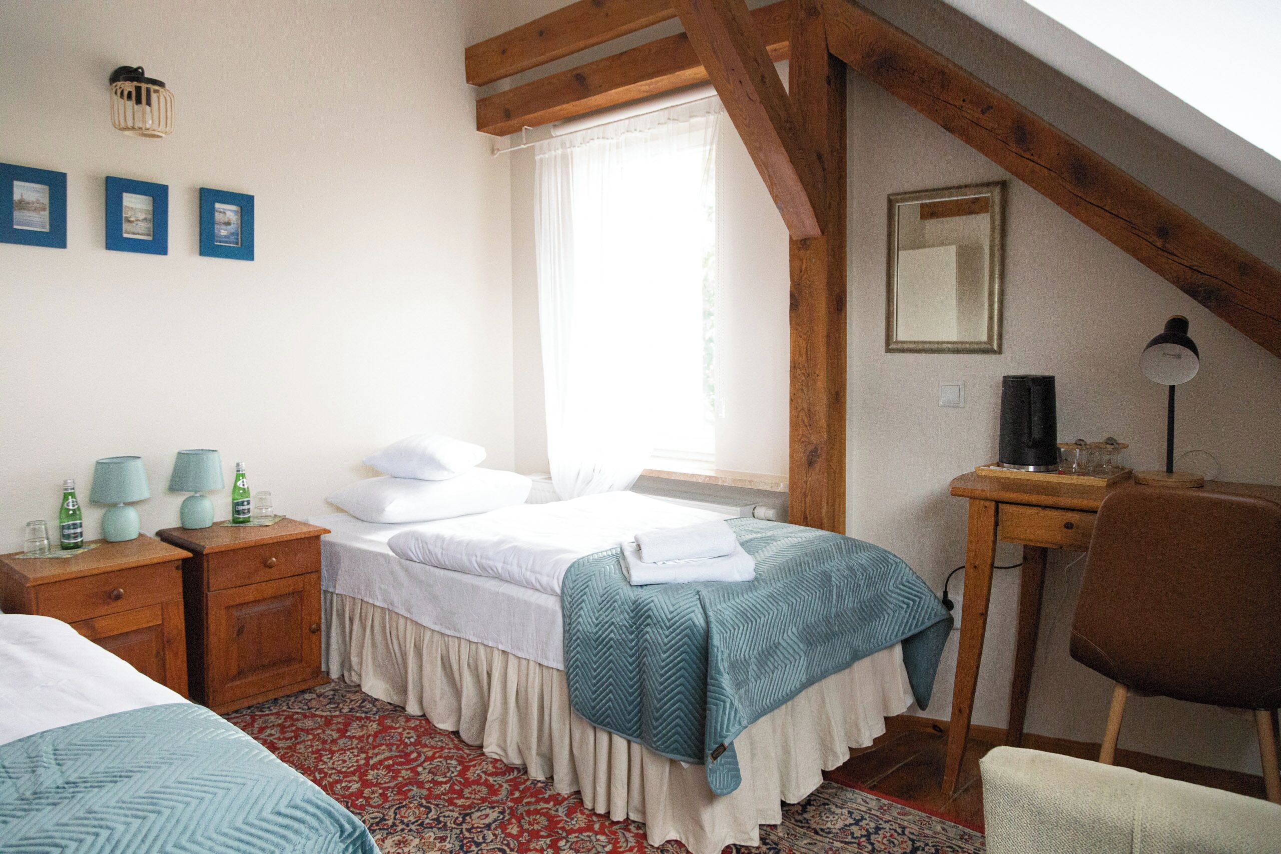 A bedroom with a bed, bedside tables, a desk, a chair, a window, and a mirror.