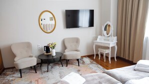 A hotel room with a bed, two armchairs, a small table with a vase of flowers, a vanity with a mirror, and a flat-screen TV on the wall. - Mleczarnia Hotel Restauracja (Suchy Las)
