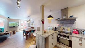 A modern kitchen with a central island, built-in oven, and a dining area with a TV in the background. - Zum Storike Nescht (Barr)