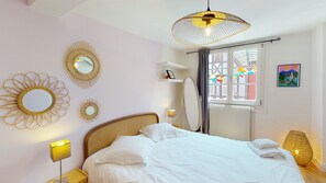 A bedroom with a bed, bedside lamps, a window with curtains, and wall decorations.